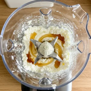 Blending cottage cheese, maple syrup, and vanilla for creamy ice cream base

