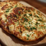 Golden-brown cottage cheese flatbreads topped with fresh chopped herbs, served on a wooden cutting board.