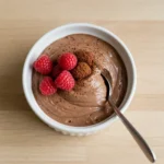 Creamy chocolate cottage cheese mousse in a white bowl topped with raspberries and cocoa powder