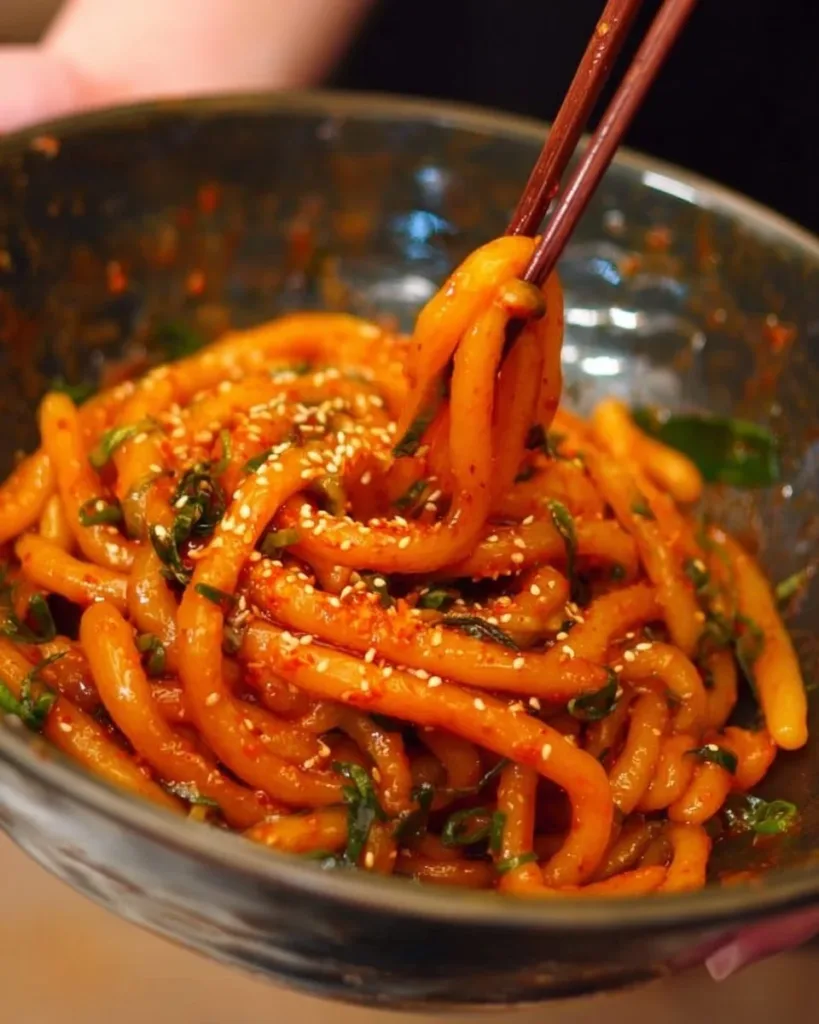 Bowl of spicy potato noodles garnished with herbs and spices